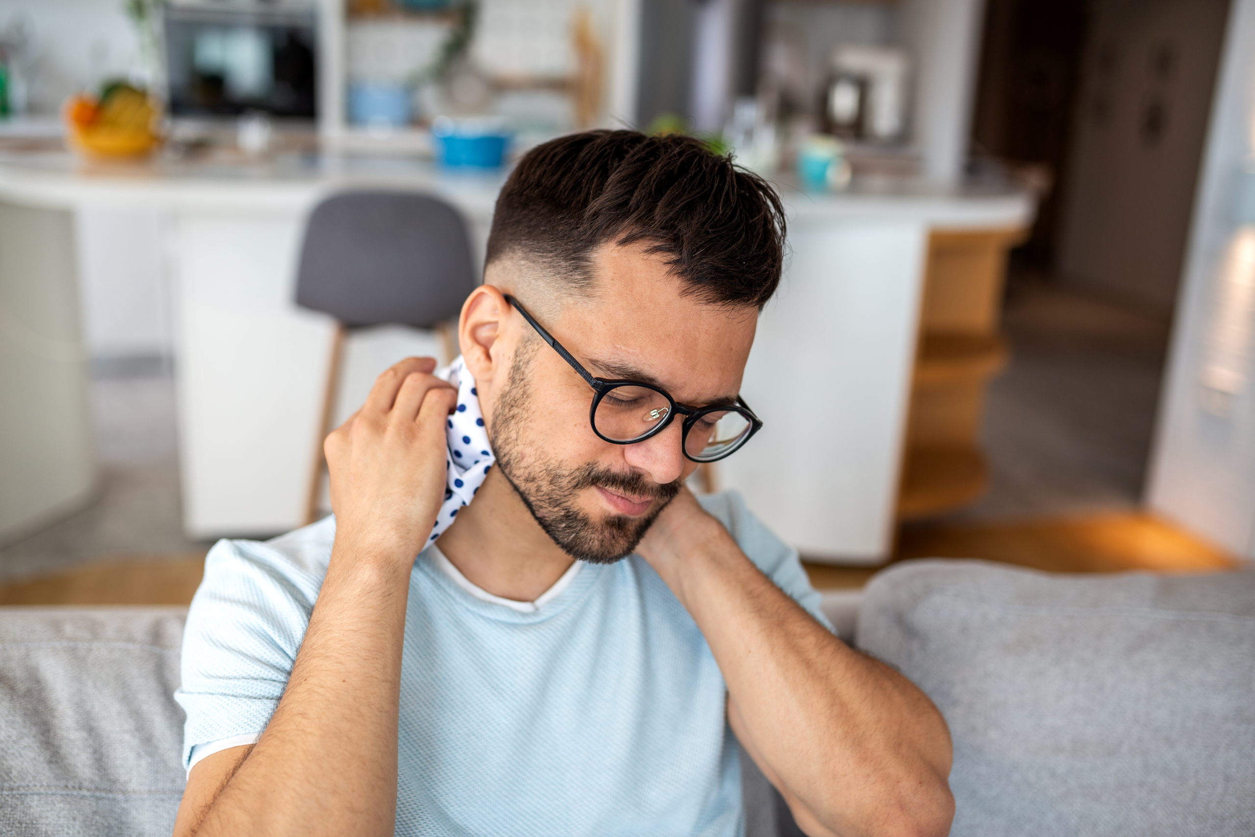 young man sitting on a sofa and using an ice pack for neck young man sitting on a sofa and using an ice pack for neck