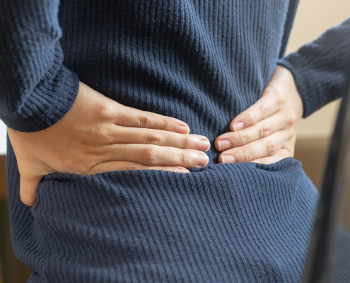An Asian woman sitting at her desk experiencing back pain from computer work, highlighting the need for a targeted pain relief pad