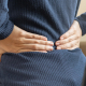 An Asian woman sitting at her desk experiencing back pain from computer work, highlighting the need for a targeted pain relief pad
