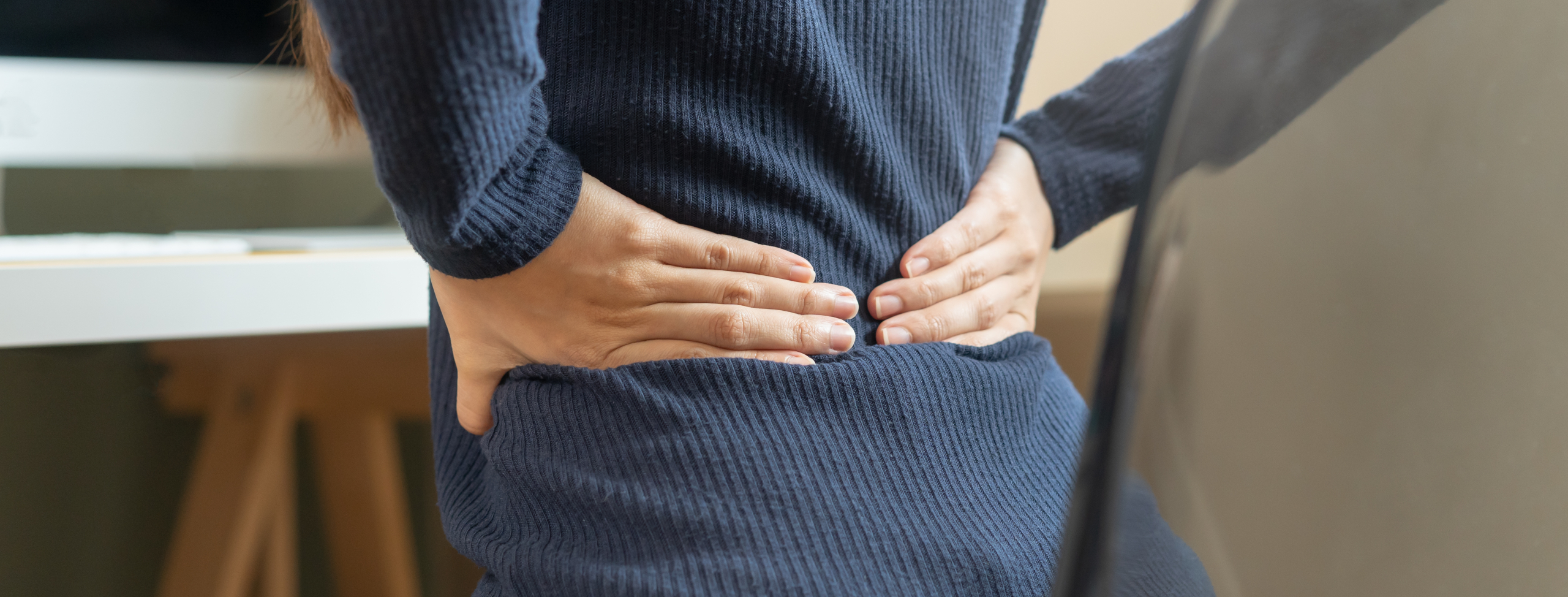 An Asian woman sitting at her desk experiencing back pain from computer work, highlighting the need for a targeted pain relief pad