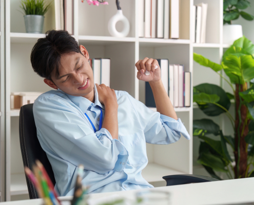 Asian man at office desk suffering from shoulder pain and muscle strain in need of muscle healing support