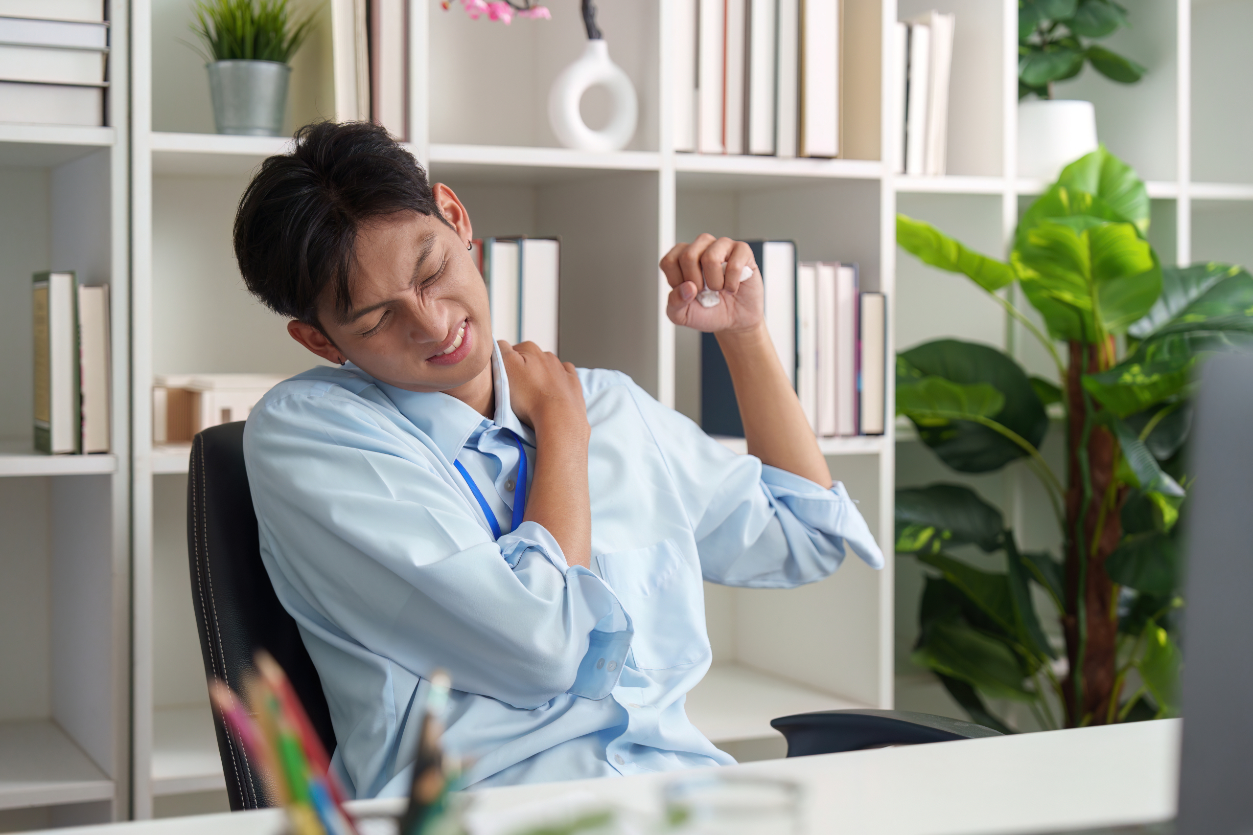 Asian man at office desk suffering from shoulder pain and muscle strain in need of muscle healing support Asian man at office desk suffering from shoulder pain and muscle strain in need of muscle healing support