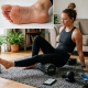 Woman using black foam roller on mat next to ice bath
