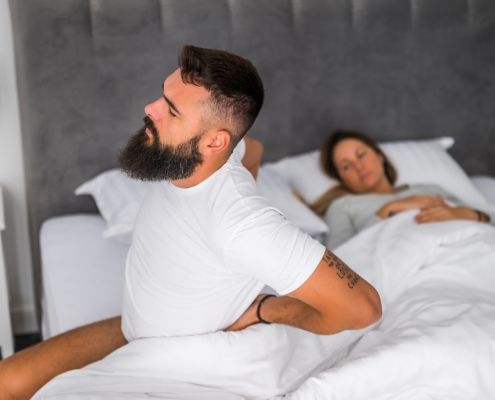 Person experiencing middle back pain while sleeping, sitting on bed and holding their thoracic spine area