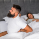 Person experiencing middle back pain while sleeping, sitting on bed and holding their thoracic spine area